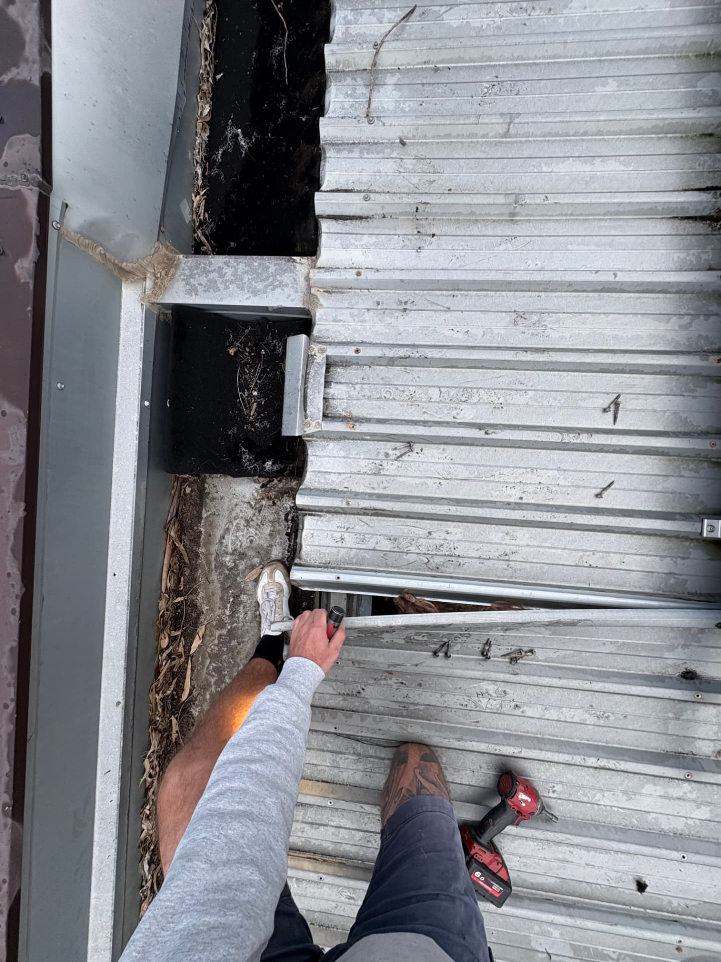 Roof plumber removing screws from metal roof sheeting beside a box gutter