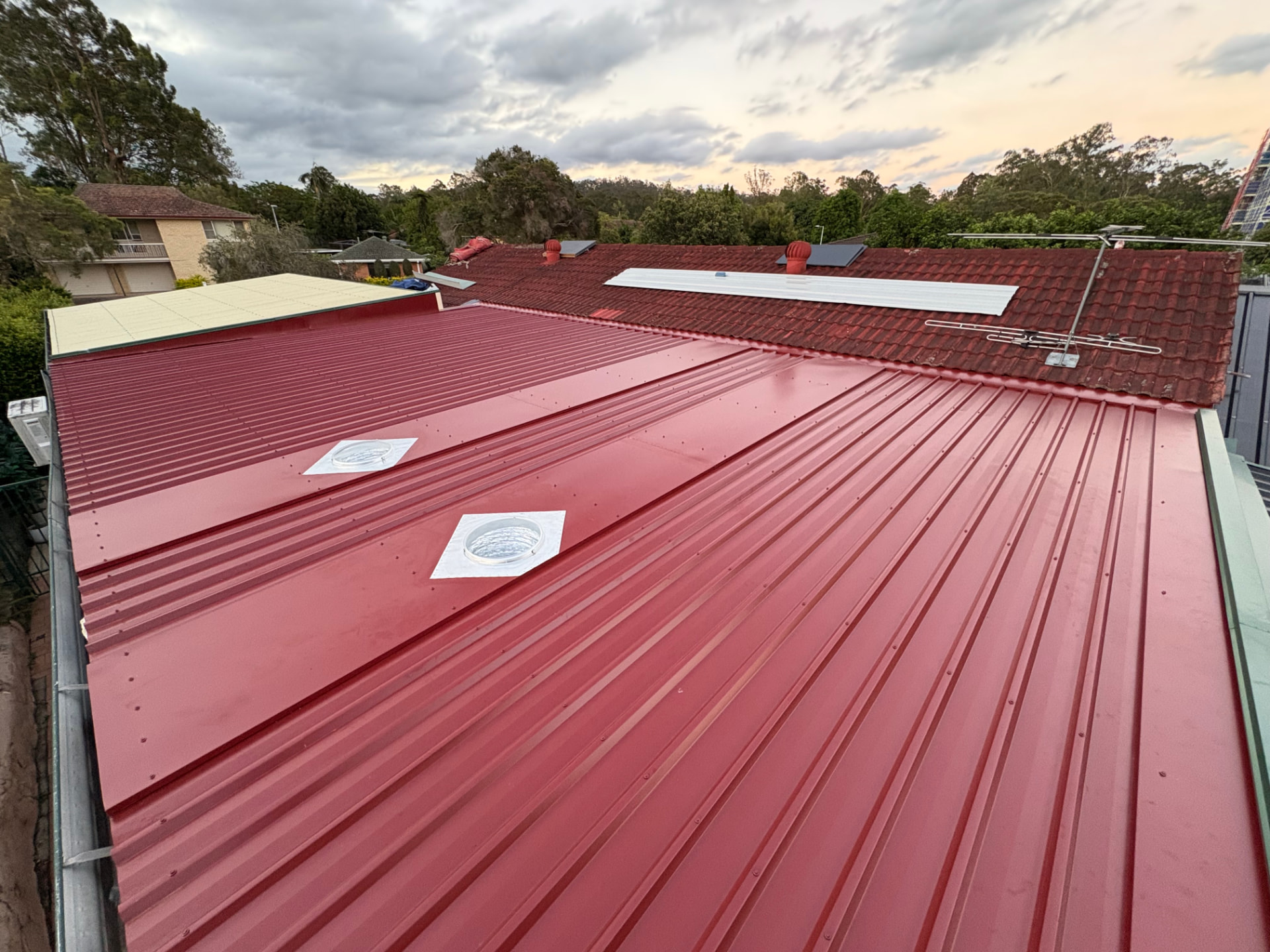 New red Colorbond roof sheeting with skylights installed alongside the original terracotta tiled roof