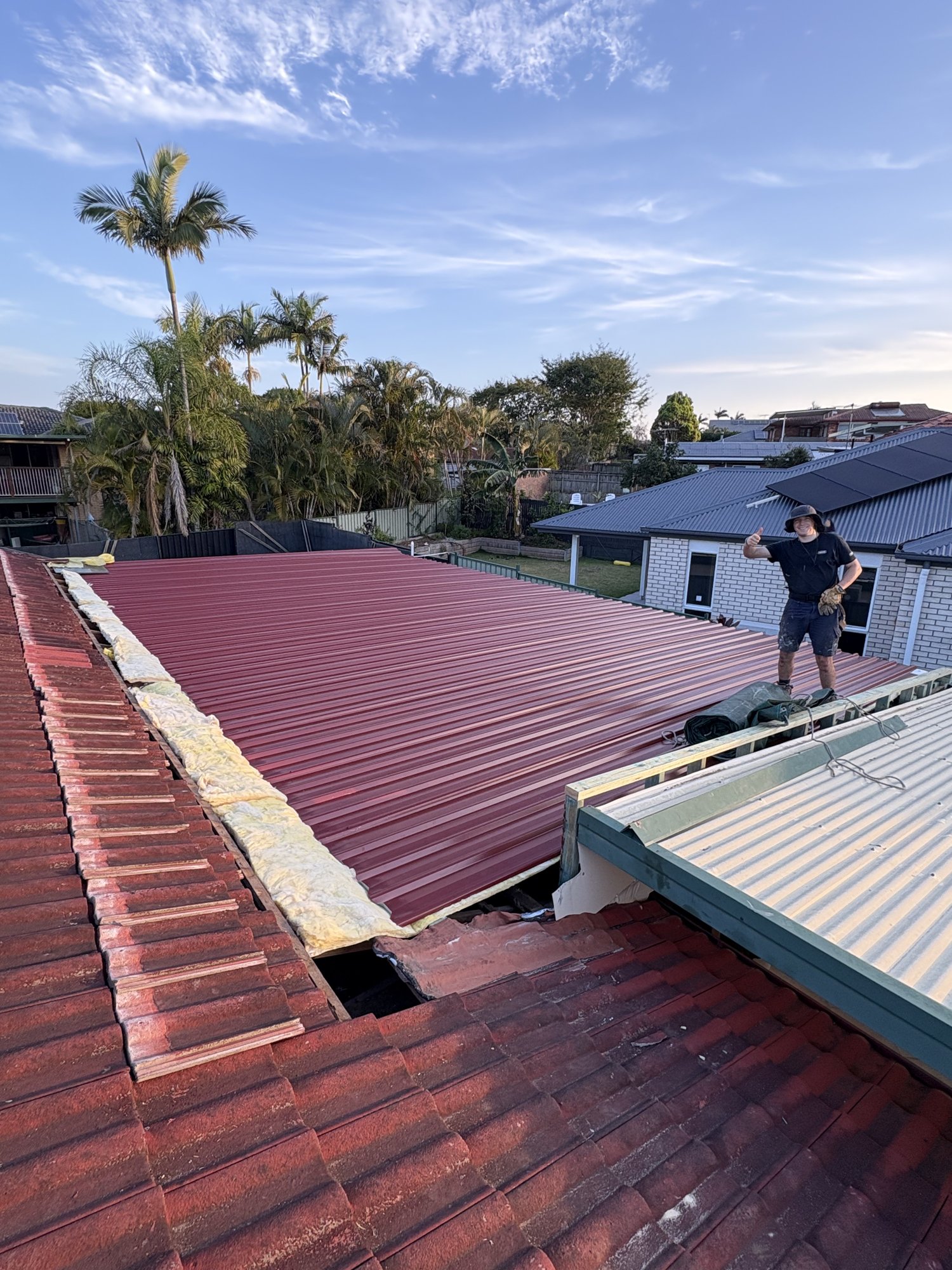 Roof plumber replacing a tiled roof section with new metal roofing in Brisbane