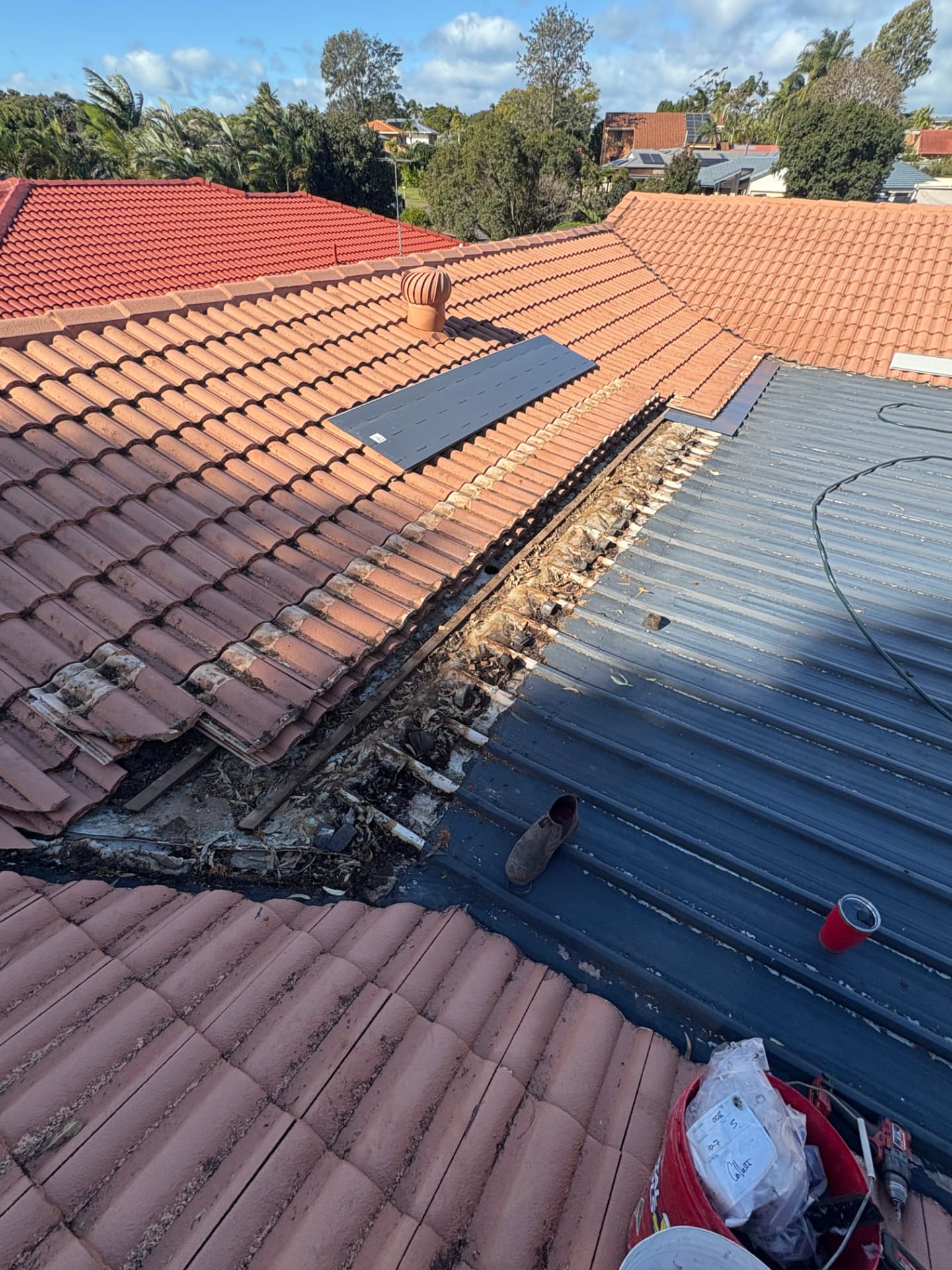 Valley gutter filled with leaf litter where the tiled roof meets the metal fly-over roof